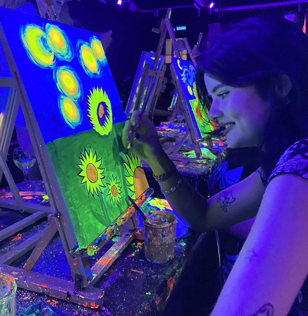 Chica en taller Wine and Art con cuadro de girasoles flúor